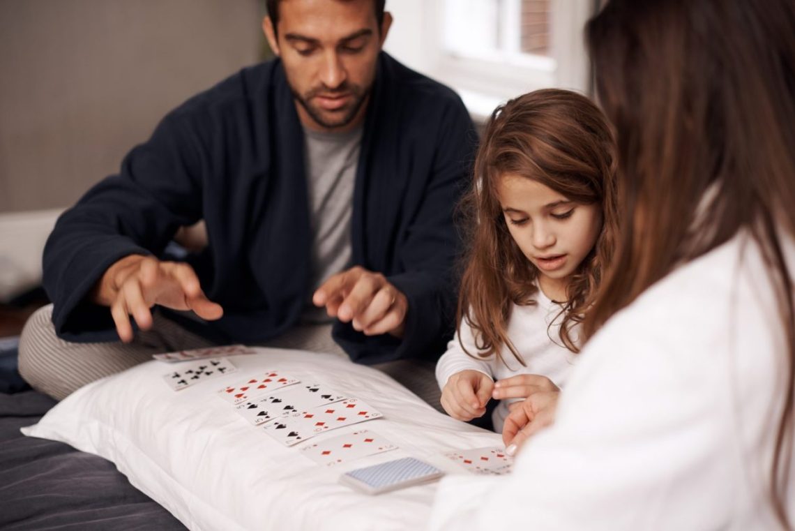 Une famille joue au jeu des 7 familles autour d’une table, avec les cartes réparties devant les joueurs.