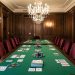 Salle parisienne élégante avec tables en feutre vert, fauteuils en velours bordeaux, boiseries sombres et lustres, dans une ambiance sobre et raffinée.